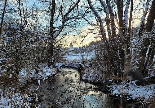 Links und Rechts Schnee bedeckte Bäume in mitten durch die Altmühl fließt und im Hintergrund Häuser und eine Kirche.