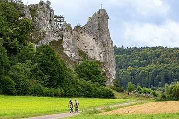 Zwei Rennradler fahren unterhalb des massiven Burgsteinfelsen gen Dollnstein