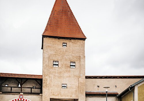 Zwei Radfahrer fahren an einem historischen Stadttor mit rotem Dach und Durchfahrt vorbei.