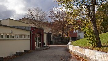 Außenansicht eines Gebäudes mit Bäumen und Gehweg im Herbst bei bewölktem Himmel.